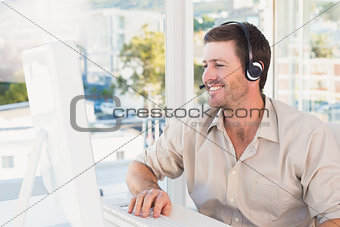 Smiling casual businessman listening to computer at desk