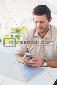 Smiling casual businessman sending a text at his desk