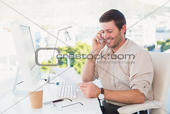 Smiling businessman making a call and reading a document