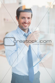 Smiling businessman holding tablet and disposable cup looking out the window