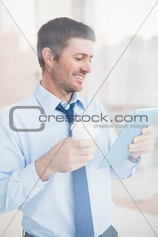 Smiling businessman using tablet holding disposable cup seen through window