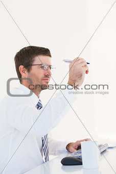Businessman holding pen up at desk