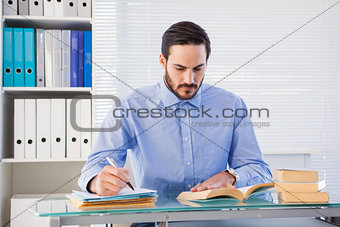 Businessman reading book while writing at his desk