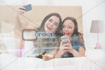 Pretty friends taking a selfie on bed