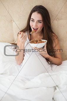 Pregnant brunette eating cereal in bed