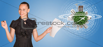 Beautiful businesswoman holding blank paper sheet and felt pen ready to use.  Beside is miniature Earth with trees, houses etc. on it