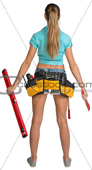 Pretty girl in shorts, shirt and tool belt with tools. Full length rear view