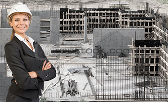 Beautiful businesswoman in helmet standing with crossed arms. Construction site as backdrop