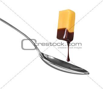 a piece of caramel chocolate drops on a spoon on a white backgro