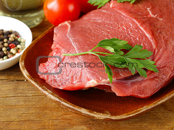 fresh raw beef meat with pepper and herbs on wooden plate