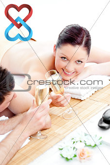 Composite image of young couple lying on a massage table and drinking champagne
