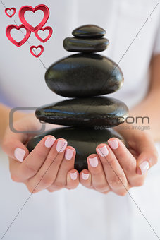 Composite image of beauty therapist holding pile of stones for massage
