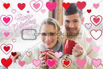 Composite image of loving couple in winter clothing with coffee cups against window