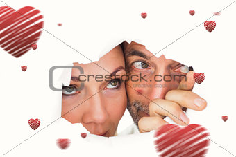 Composite image of couple looking through torn paper