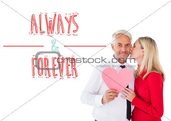 Composite image of handsome man holding paper heart getting a kiss from wife