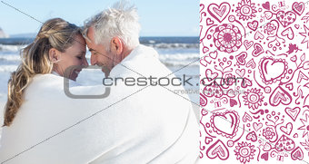 Composite image of couple sitting on the beach under blanket smiling at each other