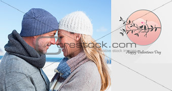 Composite image of attractive couple smiling at each other on the beach in warm clothing