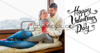 Composite image of loving couple in winter wear with cups against cabin window
