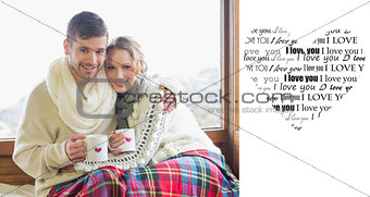 Composite image of loving couple in winter wear with cups against window
