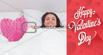 Composite image of woman lying in bed next to a fluffy heart pillow