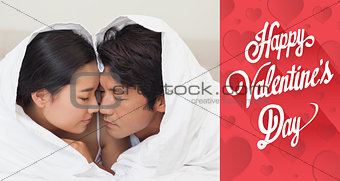 Composite image of happy couple lying on bed together under the duvet