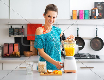 Portrait of happy fitness young woman making pumpkin smoothie in
