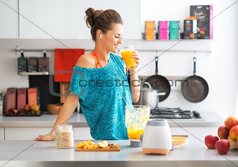 Happy fitness young woman drinking pumpkin smoothie in kitchen