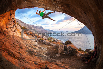Male rock climber climbing along a roof in a cave at sunset