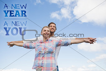 Composite image of happy couple standing outside with arms stretched