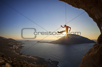 Rock climber hanging on rope while lead climbing at sunset, with Telendos island in background