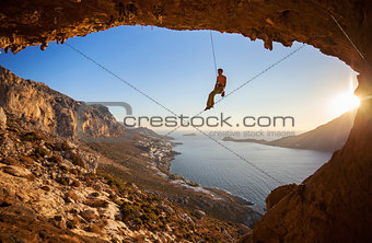 Rock climber hanging on rope while lead climbing at sunset, with Telendos island in background