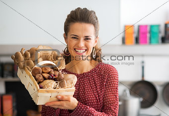 Portrait of smiling young housewife showing basket with mushroom