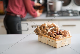 Closeup on basket with mushrooms on table and young housewife in