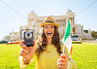 Happy young woman showing italian flag and photo camera while on
