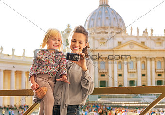 Happy mother and baby girl checking photos in camera in front of