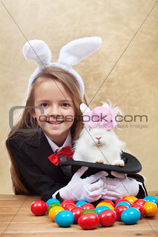 Happy magician girl holding cute bunny in magic hat