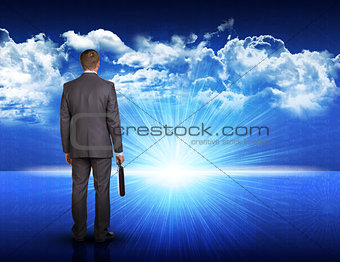 Businessman standing against blue landscape with rising sun