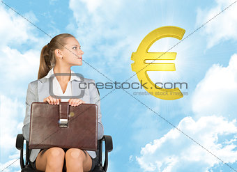 Businesswoman sitting on office chair, looking up at euro sign in the air