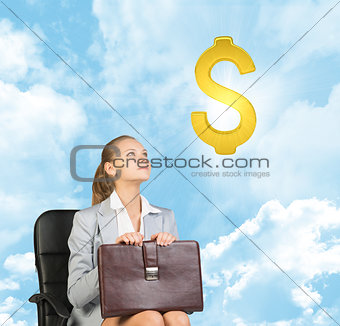 Businesswoman sitting on office chair, looking up at dollar sign in the air