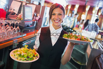 Pretty barmaid holding plates of salads