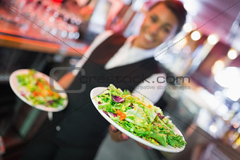 Pretty barmaid holding plates of salads