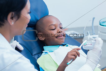 Female dentist teaching boy how to brush teeth