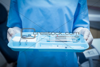 Mid section of dentist in blue scrubs holding tray of tools