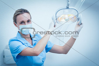 Female dentist in surgical mask adjusting light