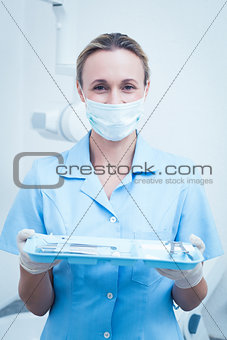 Female dentist in surgical mask holding tray of tools