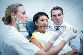 Dentist with assistant showing woman how to brush teeth