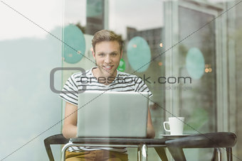 Smiling student using laptop in cafe