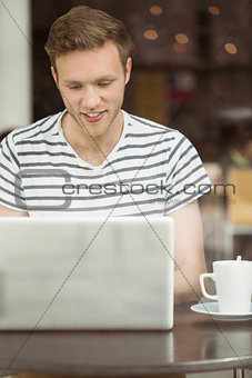 Smiling student sitting with a hot drink using laptop