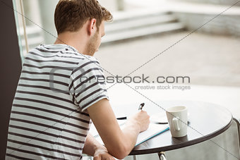 Student sitting with a hot drink and writing on notepad
