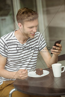 Smiling student with chocolate cake using smartphone